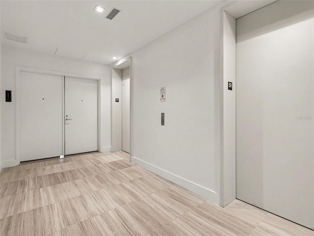 A modern hallway features light wood-look tile flooring, white walls, and two elevator doors — 3101 W BAYSHORE STREET UNIT 502, TAMPA, FL
