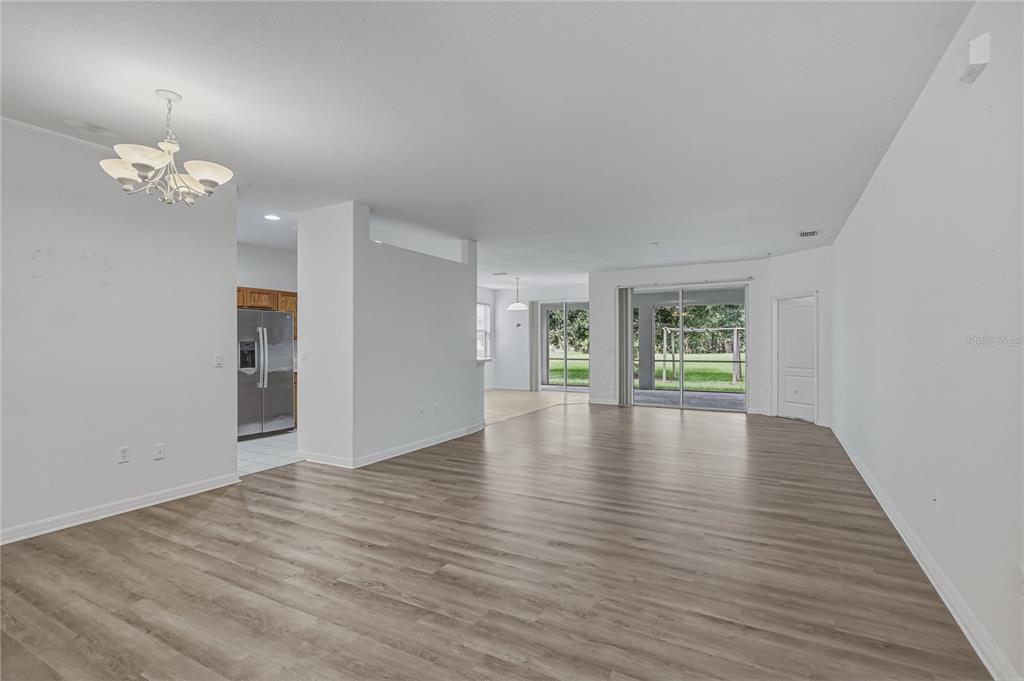 An open-concept living area features light wood-look flooring, white walls, and sliding glass patio doors — 4603 TROUT RIVER CROSSING, ELLENTON, FL