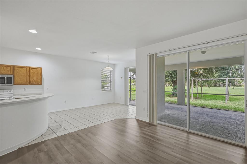 An open-concept living and dining area features wood-look flooring, tiled kitchen space, and sliding doors — 4603 TROUT RIVER CROSSING, ELLENTON, FL