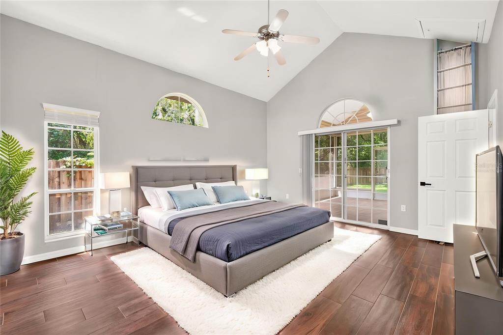 A bedroom with a vaulted ceiling, gray walls, wood-look tile floors, and a sliding glass door — 1124 NW 98TH TERRACE, GAINESVILLE, FL