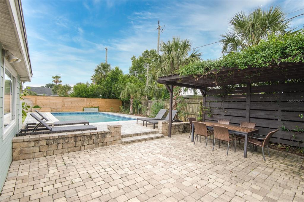 A backyard patio features a swimming pool, a wooden pergola, and a stone retaining wall — 159 SOUTHWIND (POOL HOME) CIRCLE, ST AUGUSTINE, FL