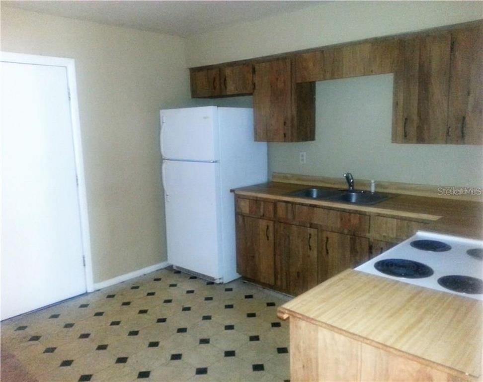 A kitchen features wood cabinets, a white refrigerator, a double sink, and patterned vinyl flooring — 1102 SOUTHERN AVENUE UNIT 1104, LAKELAND, FL