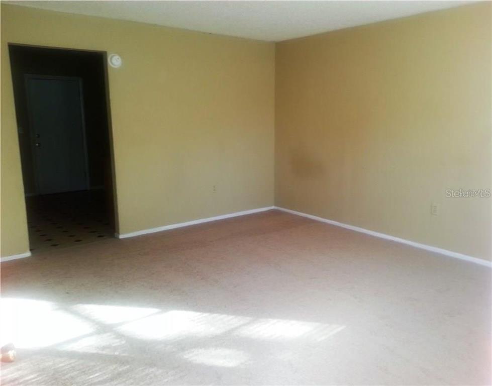 An empty room with beige walls and tan carpeting features a doorway to another area — 1102 SOUTHERN AVENUE UNIT 1104, LAKELAND, FL