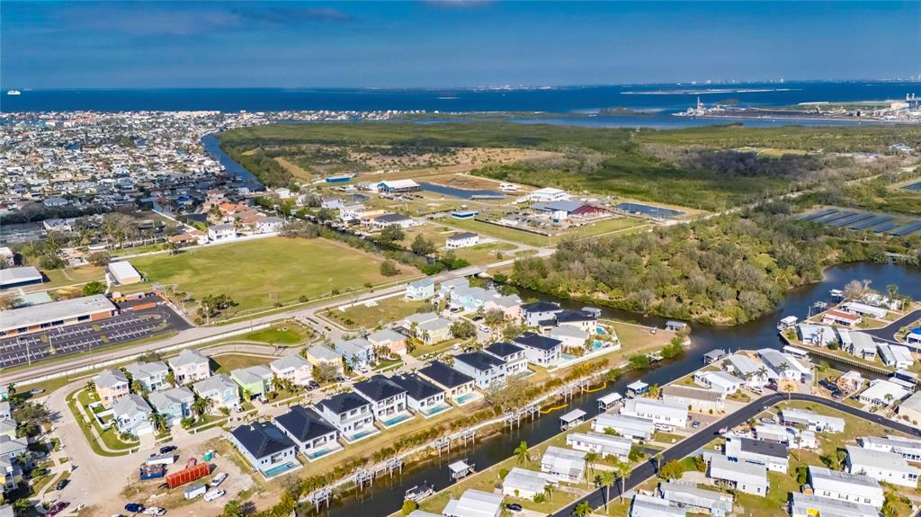 An aerial view shows a coastal neighborhood with houses, a canal, and nearby undeveloped land — 6538 SIMONE SHORES CIRCLE, APOLLO BEACH, FL