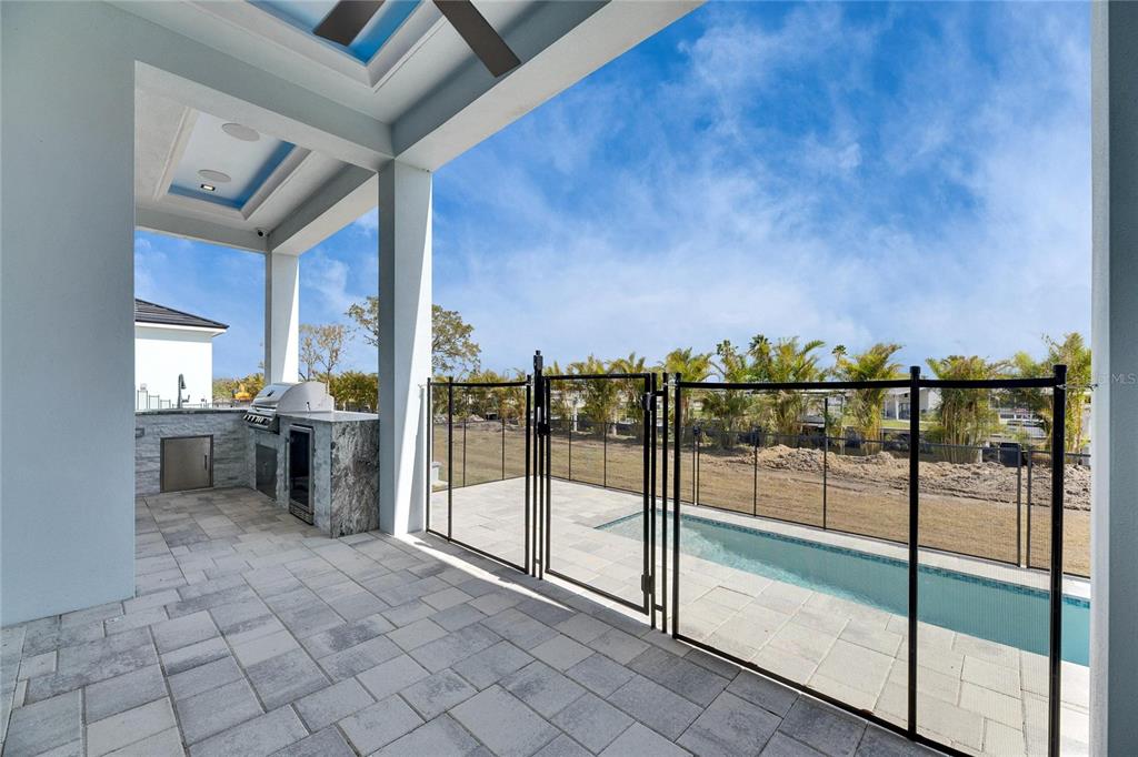 A covered patio features an outdoor kitchen, stone pavers, and a fenced pool area — 6538 SIMONE SHORES CIRCLE, APOLLO BEACH, FL