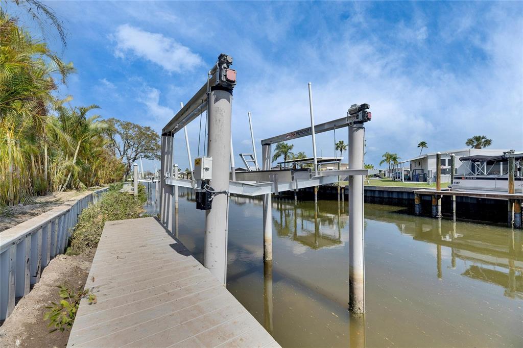 A boat lift stands over a canal next to a wooden dock and palm trees — 6538 SIMONE SHORES CIRCLE, APOLLO BEACH, FL
