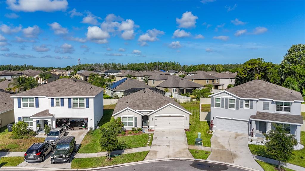 An aerial view shows three suburban houses with driveways and lawns under a blue sky — 16661 WINDMILL FORGE PASS, WIMAUMA, FL