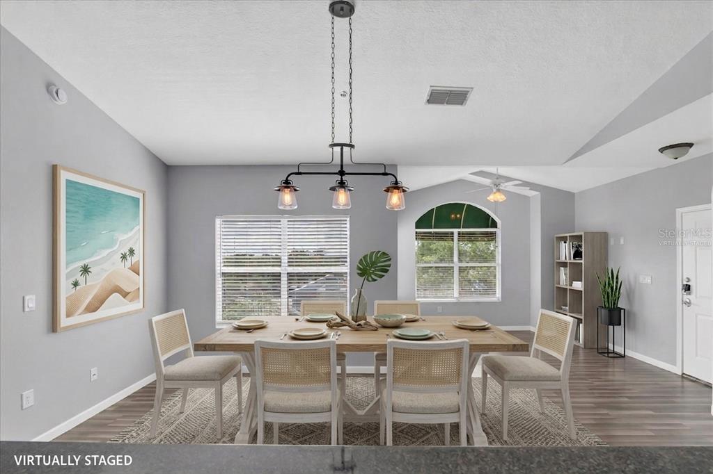 A virtually staged dining room with a wooden table, six gray chairs, and pendant lighting — 10764 70TH AVENUE UNIT 3307, SEMINOLE, FL