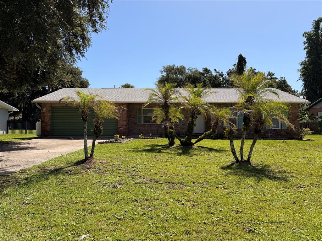 A single-story brick house features a green garage door and several palm trees out front — 2513 ORANGE TREE DRIVE, EDGEWATER, FL