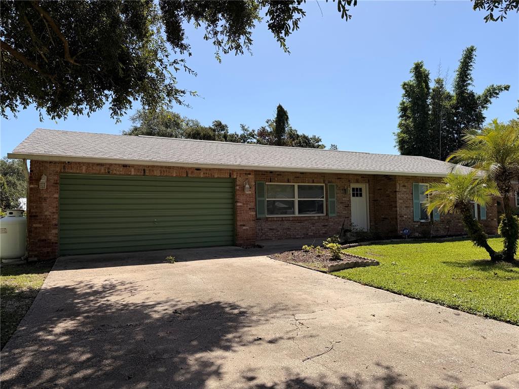A single-story brick house with a green garage door and a concrete driveway — 2513 ORANGE TREE DRIVE, EDGEWATER, FL