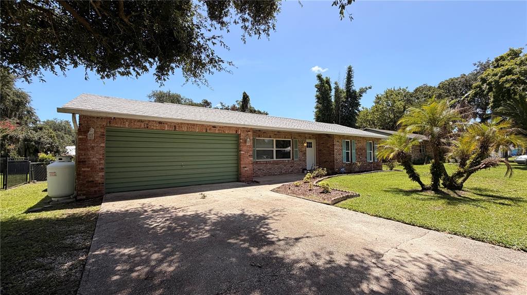 A single-story brick house features a green garage door, a concrete driveway, and palm trees — 2513 ORANGE TREE DRIVE, EDGEWATER, FL