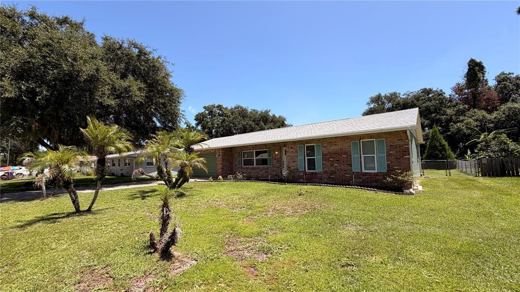 A single-story brick house with a light-colored roof and green shutters sits on a lawn — 2513 ORANGE TREE DRIVE, EDGEWATER, FL