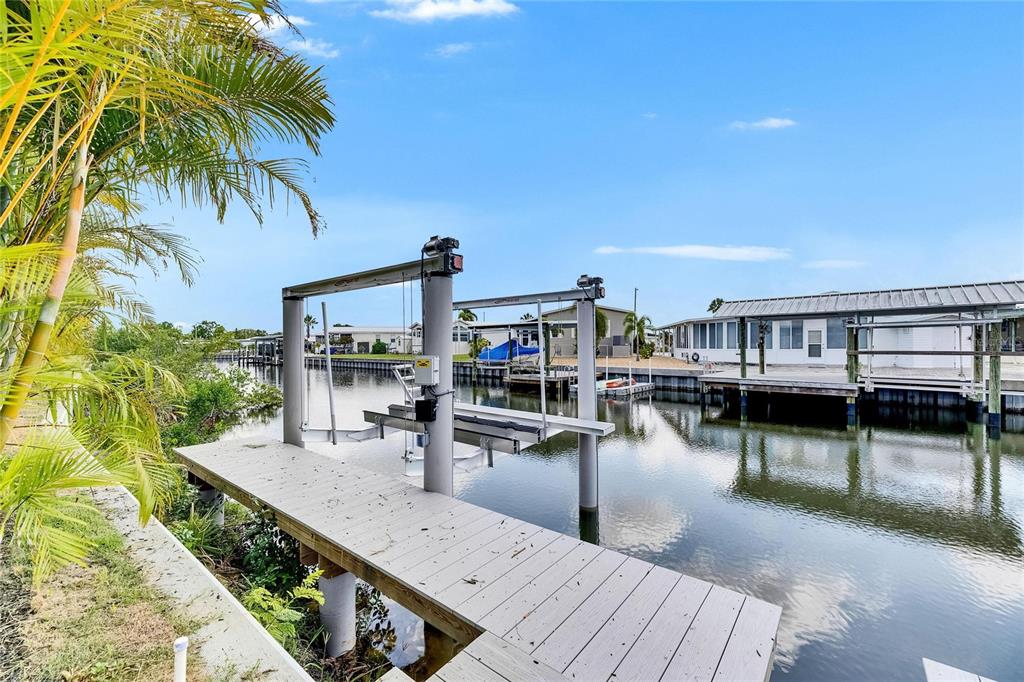 A wooden dock with a boat lift sits along a canal next to residential homes — 6526 SIMONE SHORES CIRCLE, APOLLO BEACH, FL