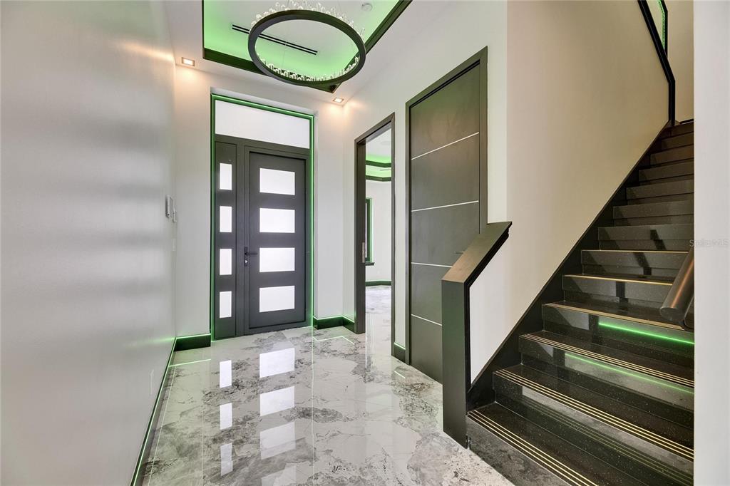 A modern entryway features a marble floor, a dark staircase with green lighting, and a door — 6526 SIMONE SHORES CIRCLE, APOLLO BEACH, FL