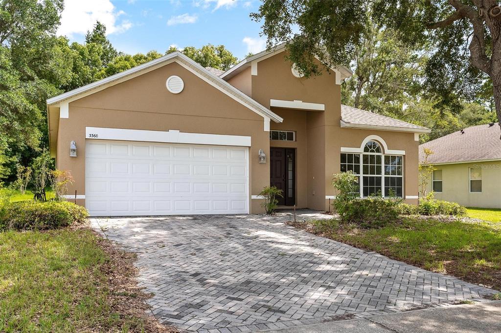 A tan, single-story house with a white garage door and a paved driveway — 3360 CREEK RUN LANE, EUSTIS, FL