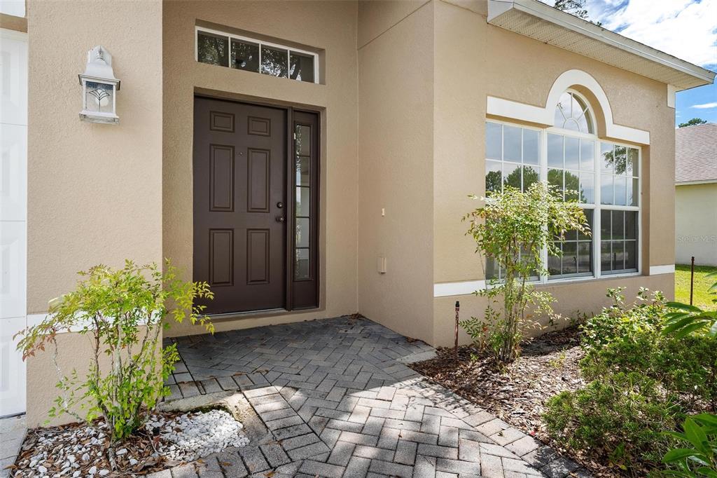 A front entryway features a dark brown door, a brick paver walkway, and a large window — 3360 CREEK RUN LANE, EUSTIS, FL
