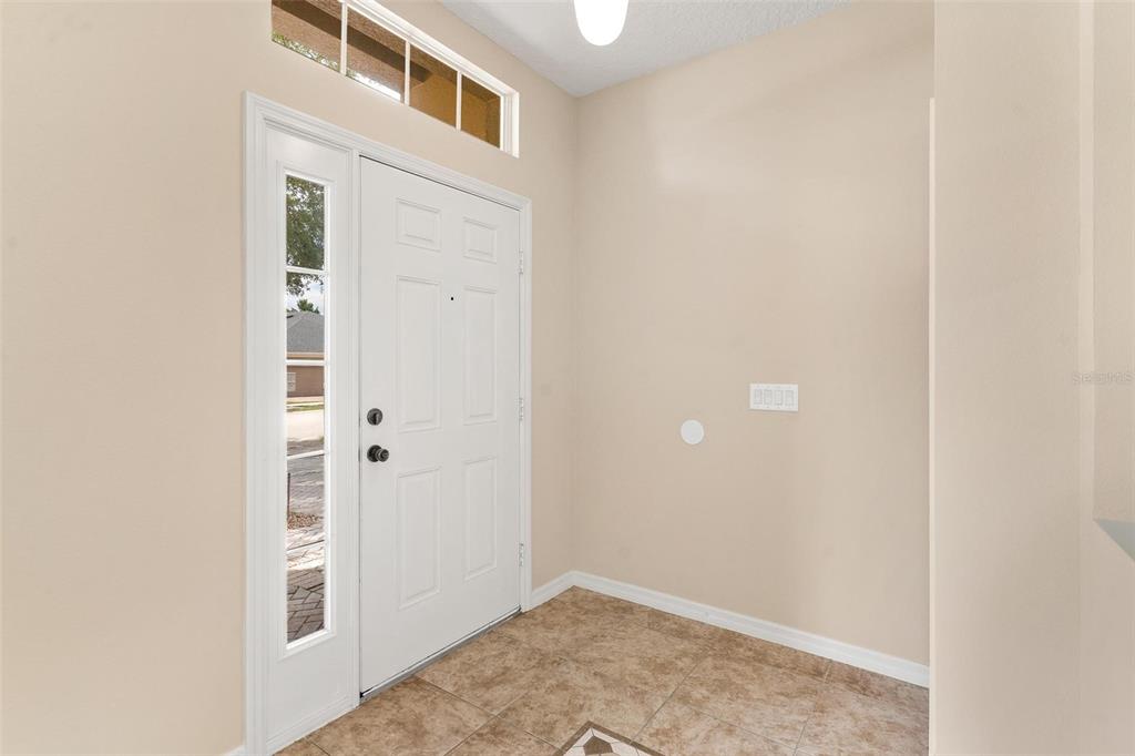 An entryway with a white front door, sidelight, transom window, and tan tile flooring — 3360 CREEK RUN LANE, EUSTIS, FL