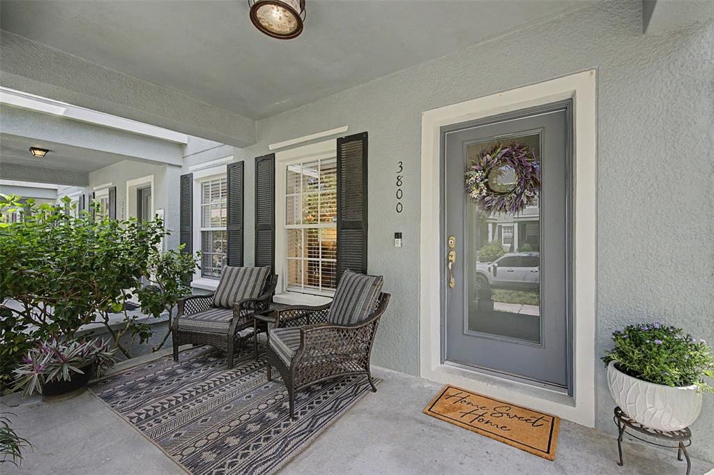 A covered front porch features two wicker chairs, a patterned rug, and a gray front door — 3800 HERLONG STREET, NEW PORT RICHEY, FL