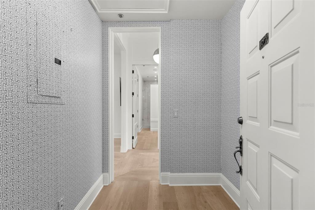 An entryway with patterned wallpaper, light wood flooring, and a white door with a number — 1602 ALABAMA DRIVE UNIT 107, WINTER PARK, FL