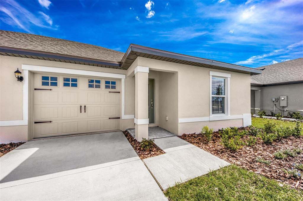 A beige single-story house exterior features a two-car garage, a front entryway, and a window — 3208 SEVILLE STREET, LAKE ALFRED, FL