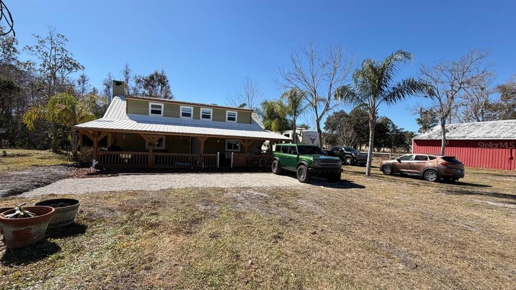 A green house with a metal roof and a large front porch sits on gravel — 445 S STATE ROAD 415, OSTEEN, FL