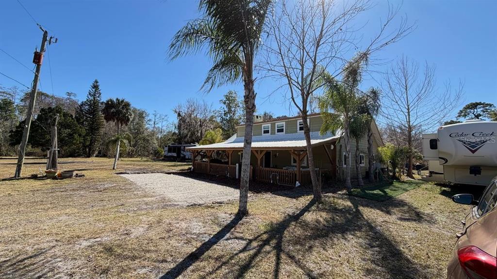 A green house with a metal roof and a wrap-around porch sits on a grassy lot — 445 S STATE ROAD 415, OSTEEN, FL
