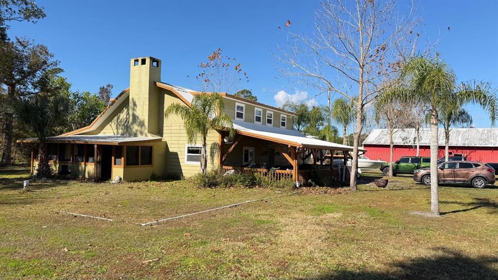 A yellow two-story house with a metal roof, large chimney, and a wrap-around porch — 445 S STATE ROAD 415, OSTEEN, FL