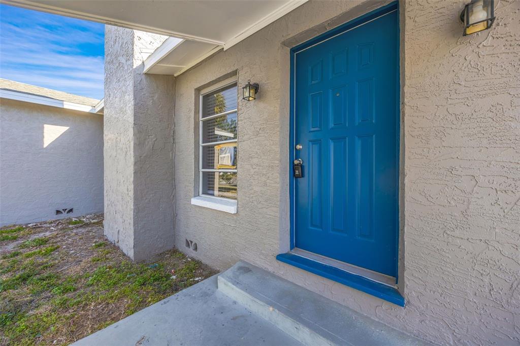 A blue front door is set into a gray stucco exterior wall next to a window — 4512 HAITI DRIVE, HERNANDO BEACH, FL