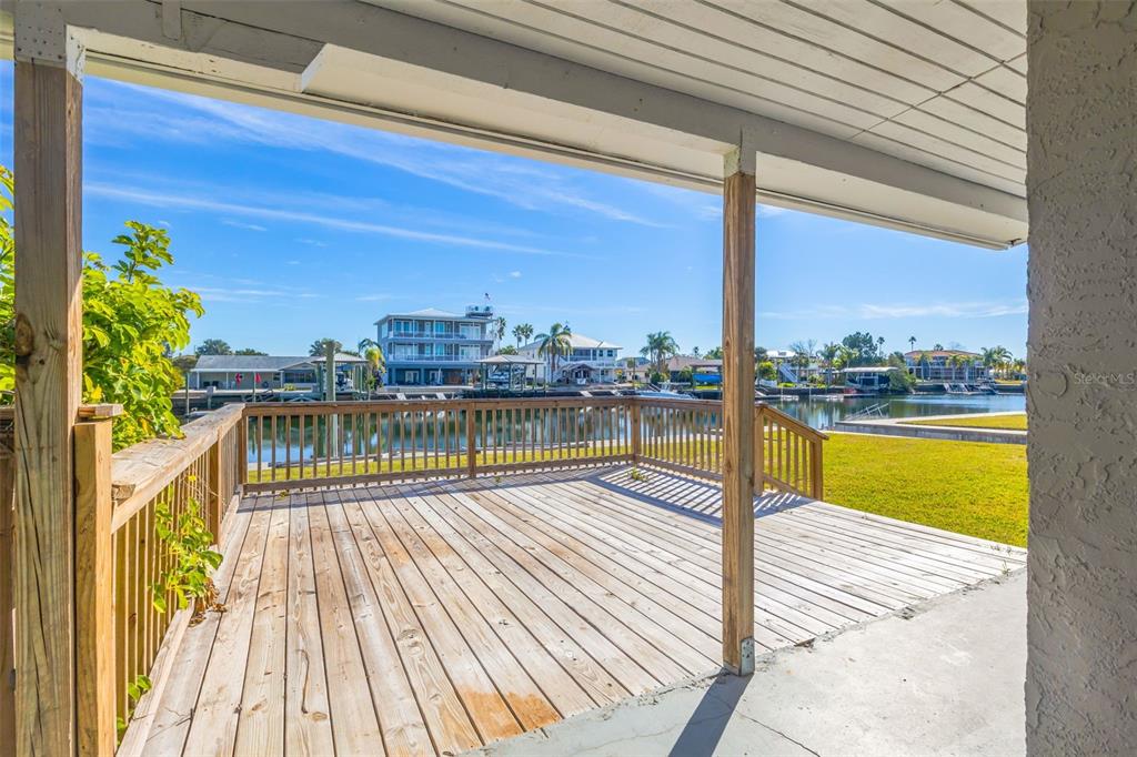 A wooden deck overlooks a canal with houses and palm trees in the background — 4512 HAITI DRIVE, HERNANDO BEACH, FL