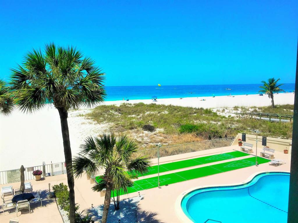 An elevated view of a beach, swimming pool, and shuffleboard courts from a balcony — 5000 GULF BOULEVARD UNIT 303, ST PETE BEACH, FL