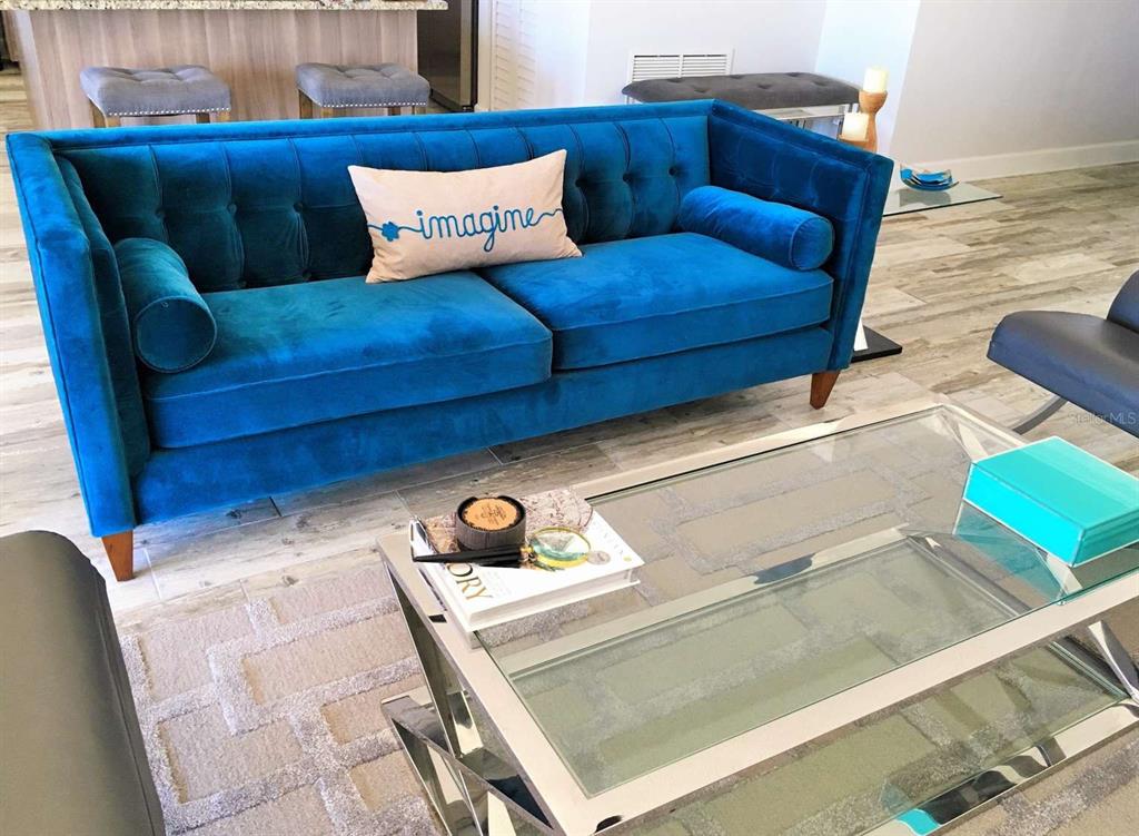 A blue tufted velvet sofa sits in a living room with a glass coffee table — 5000 GULF BOULEVARD UNIT 303, ST PETE BEACH, FL