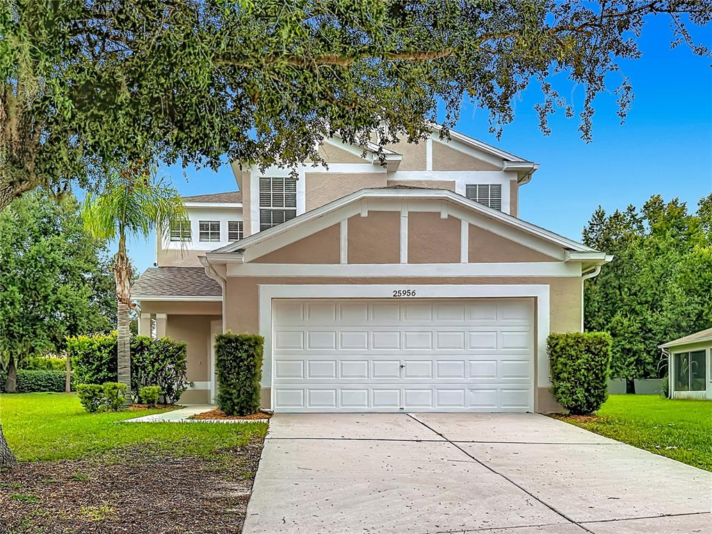 A two-story suburban house features a tan exterior, a white garage door, and a driveway — 25956 TERRAWOOD LOOP, LAND O LAKES, FL