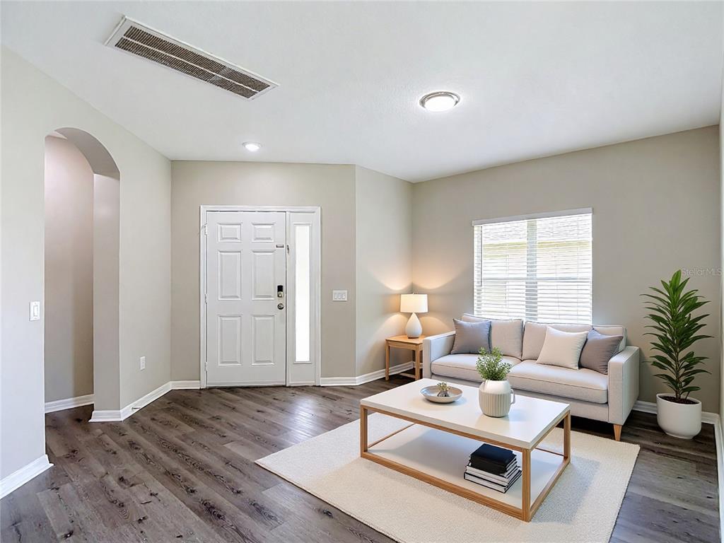 A living room features wood-look flooring, a white sofa, a coffee table, and an entryway door — 25956 TERRAWOOD LOOP, LAND O LAKES, FL