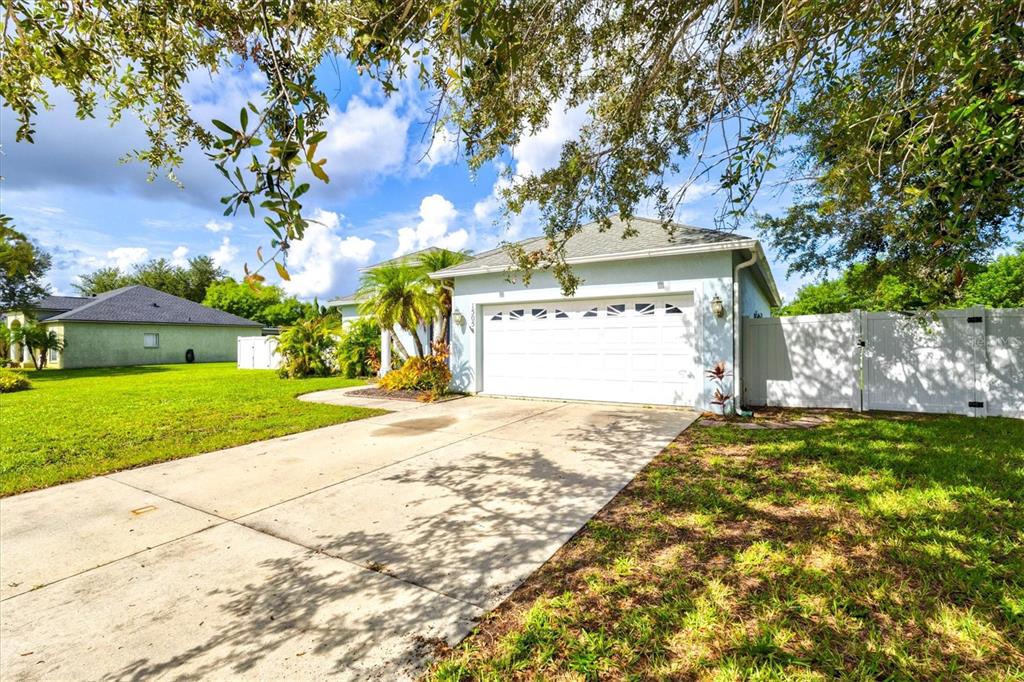 A light blue house with a white garage door and a concrete driveway under trees — 1505 22ND AVENUE W, PALMETTO, FL