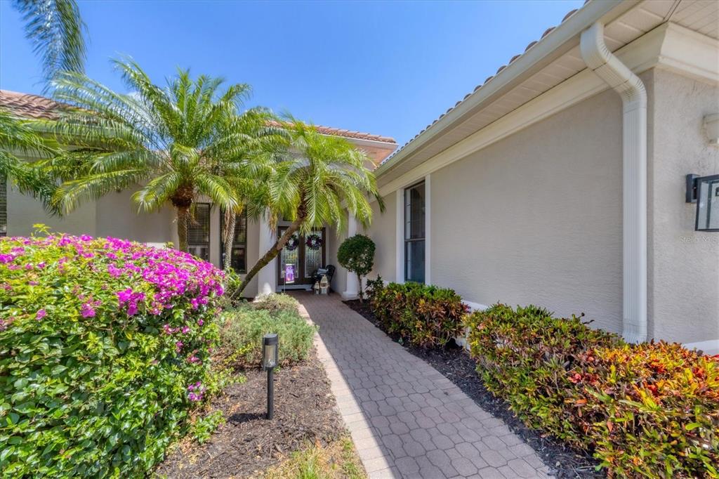 A paved walkway leads to the front entrance of a house with palm trees — 13853 SIENA LOOP, LAKEWOOD RANCH, FL