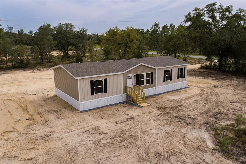 An aerial view of a tan manufactured home with a shingled roof on a sandy lot — 11091 NE 80 STREET, BRONSON, FL