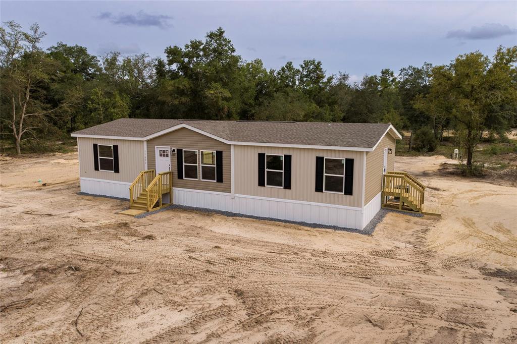 A tan manufactured home with black shutters sits on a cleared, sandy lot — 11091 NE 80 STREET, BRONSON, FL