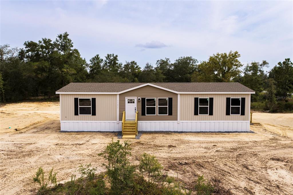 A single-story manufactured home with tan siding sits on a cleared, sandy lot — 11091 NE 80 STREET, BRONSON, FL