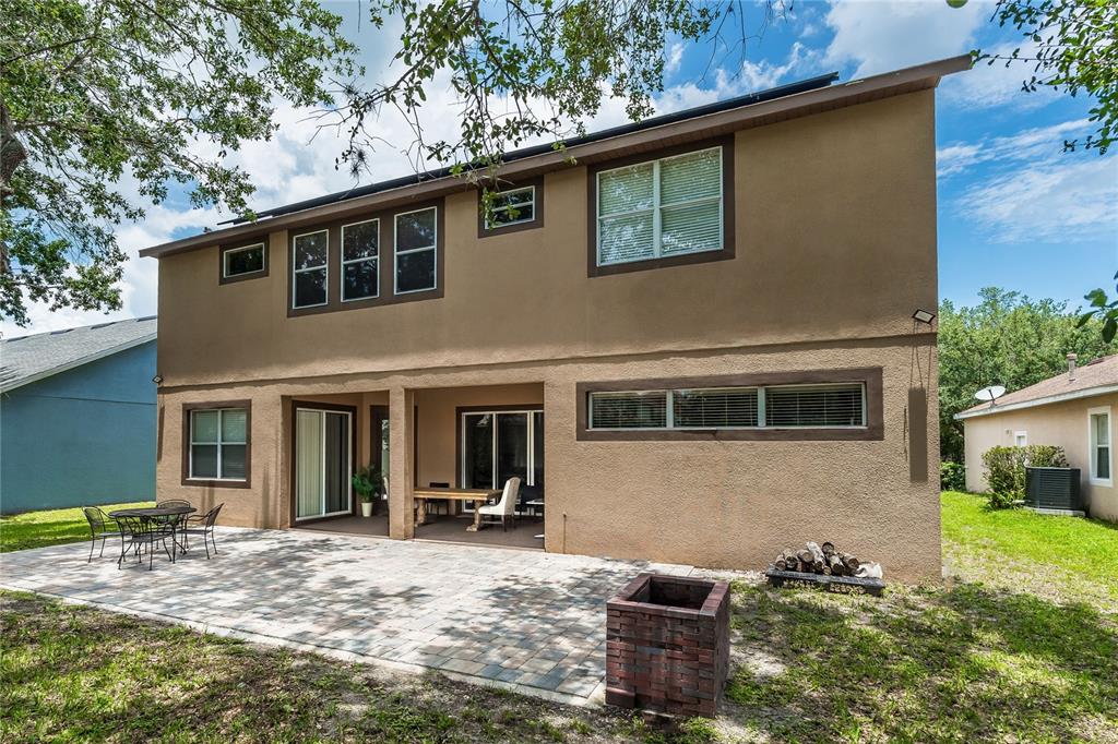 The rear exterior of a two-story stucco house features a paved patio and fire pit — 4642 RIVER GEM AVENUE, WINDERMERE, FL