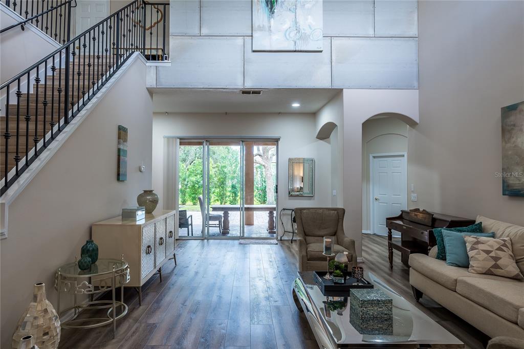 A living room features wood-look flooring, a staircase with black railings, and glass sliding doors — 4642 RIVER GEM AVENUE, WINDERMERE, FL