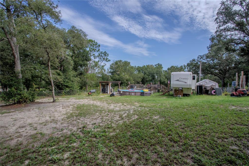 A grassy yard features a swimming pool, a camper, and a small wooden structure — 1776 ANDERSON LANE, LADY LAKE, FL