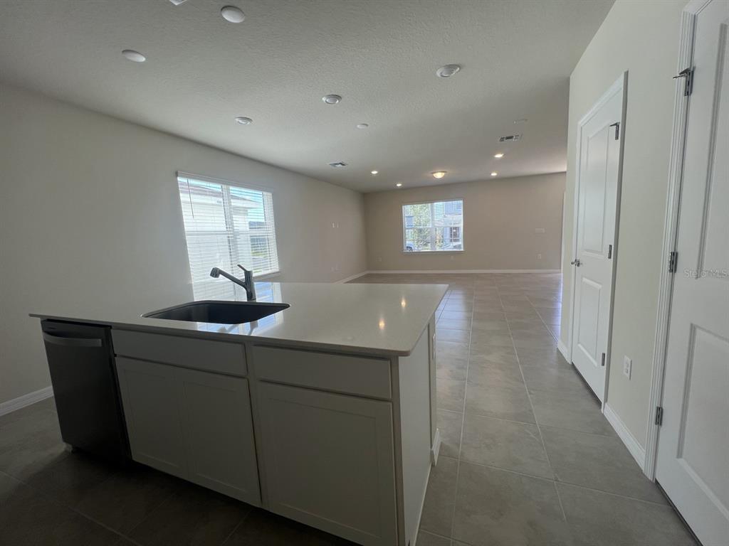 A kitchen island with a sink and dishwasher sits in an open-concept room with tile flooring — 3355 VINE LEAF STREET, APOPKA, FL
