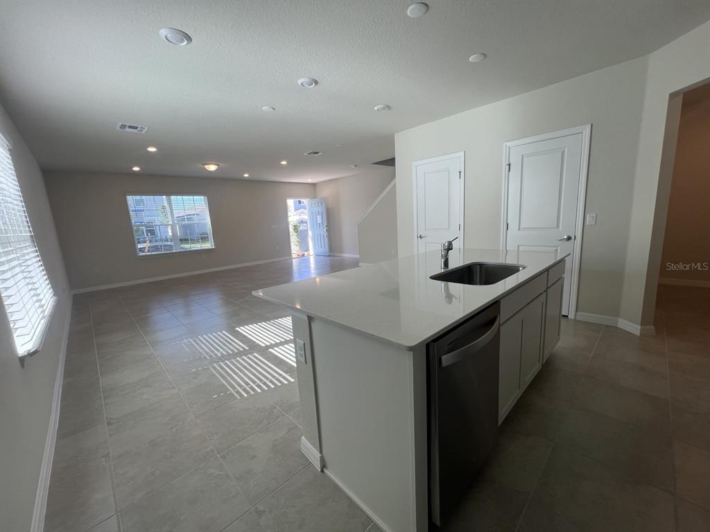 A kitchen island with a sink and dishwasher overlooks an open-concept living area with tile flooring — 3355 VINE LEAF STREET, APOPKA, FL
