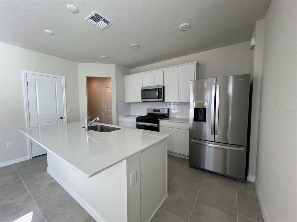 A modern kitchen features white cabinets, stainless steel appliances, and a large quartz-topped island — 3355 VINE LEAF STREET, APOPKA, FL