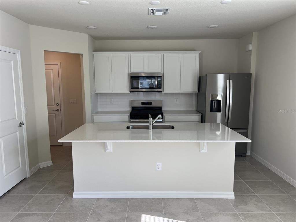 A kitchen features white cabinets, stainless steel appliances, a quartz island, and light tile flooring — 3355 VINE LEAF STREET, APOPKA, FL