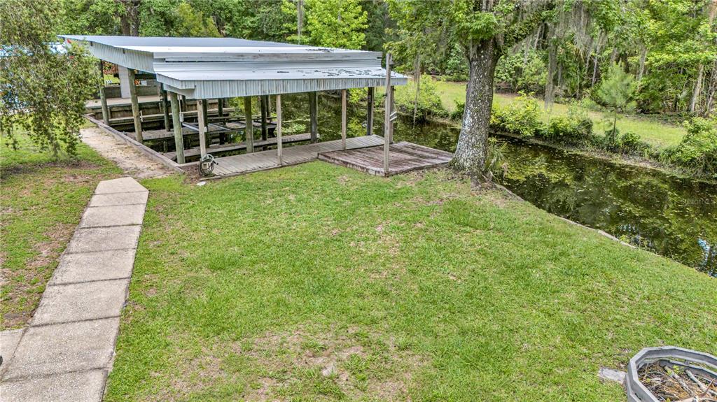 A single-story house with a metal roof and a detached garage sits on a lawn — 22308 BLUE CREEK LODGE ROAD, ASTOR, FL