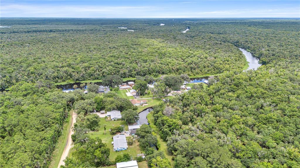 A single-story house with a metal roof, a detached carport, and a large grassy yard — 22308 BLUE CREEK LODGE ROAD, ASTOR, FL