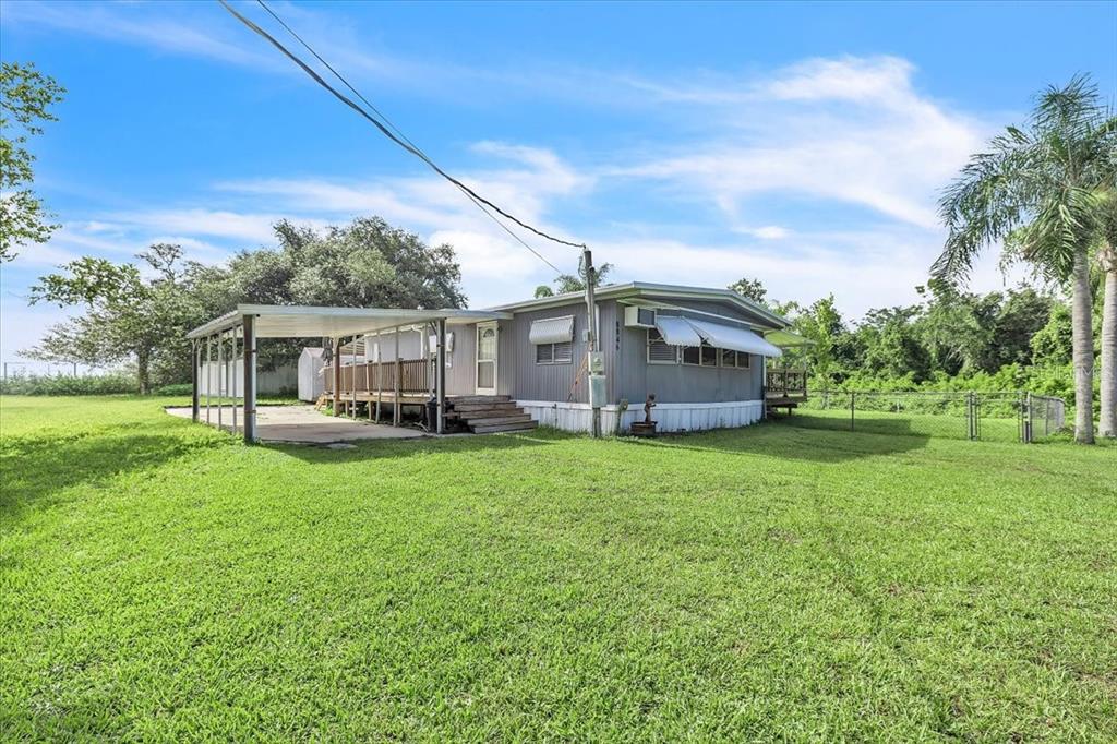 A single-story manufactured home with a carport and wooden deck sits on a grassy lot — 8846 SW COULTER ROAD, ARCADIA, FL