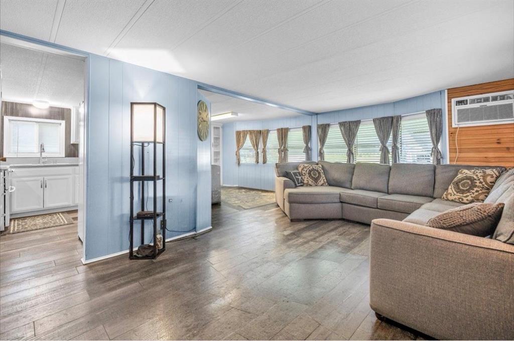 A living room with light blue paneled walls, wood-look flooring, and a large sectional sofa — 8846 SW COULTER ROAD, ARCADIA, FL
