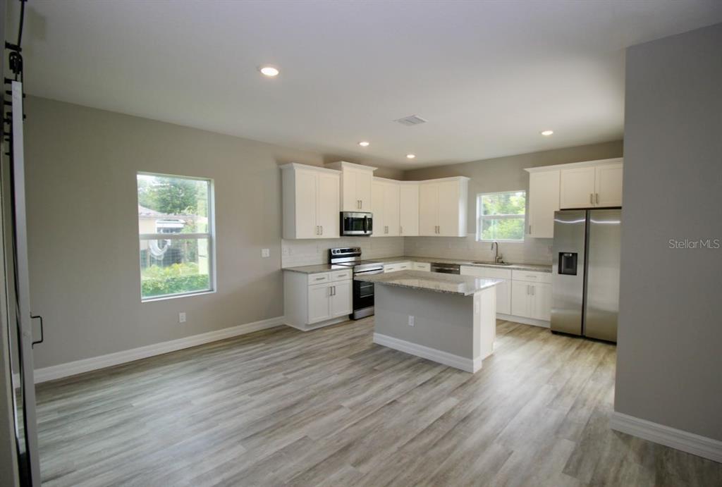 A kitchen with white cabinets, stainless steel appliances, a center island, and light wood flooring — 4175 POLYNESIA ROAD, NORTH PORT, FL